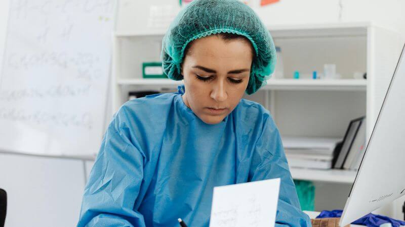 Female doctor in scrub suit writing notes.